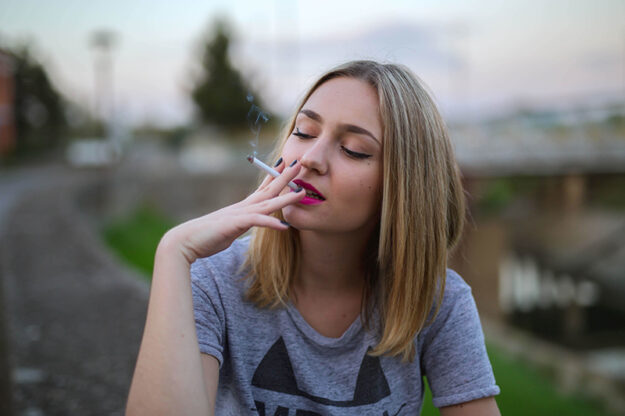 Emily in haar grijze shirt doet aan roken midden op straat in Amsterdam