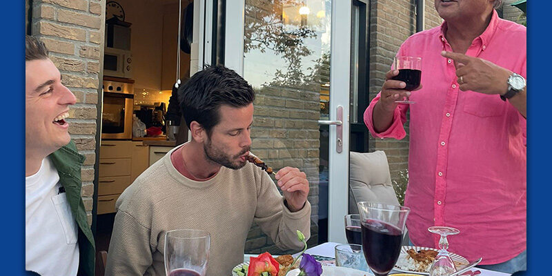 Mensen zitten aan tafel in de tuin en genieten van de zomer, 1 man vertelt over mondgezondheid in de zomer
