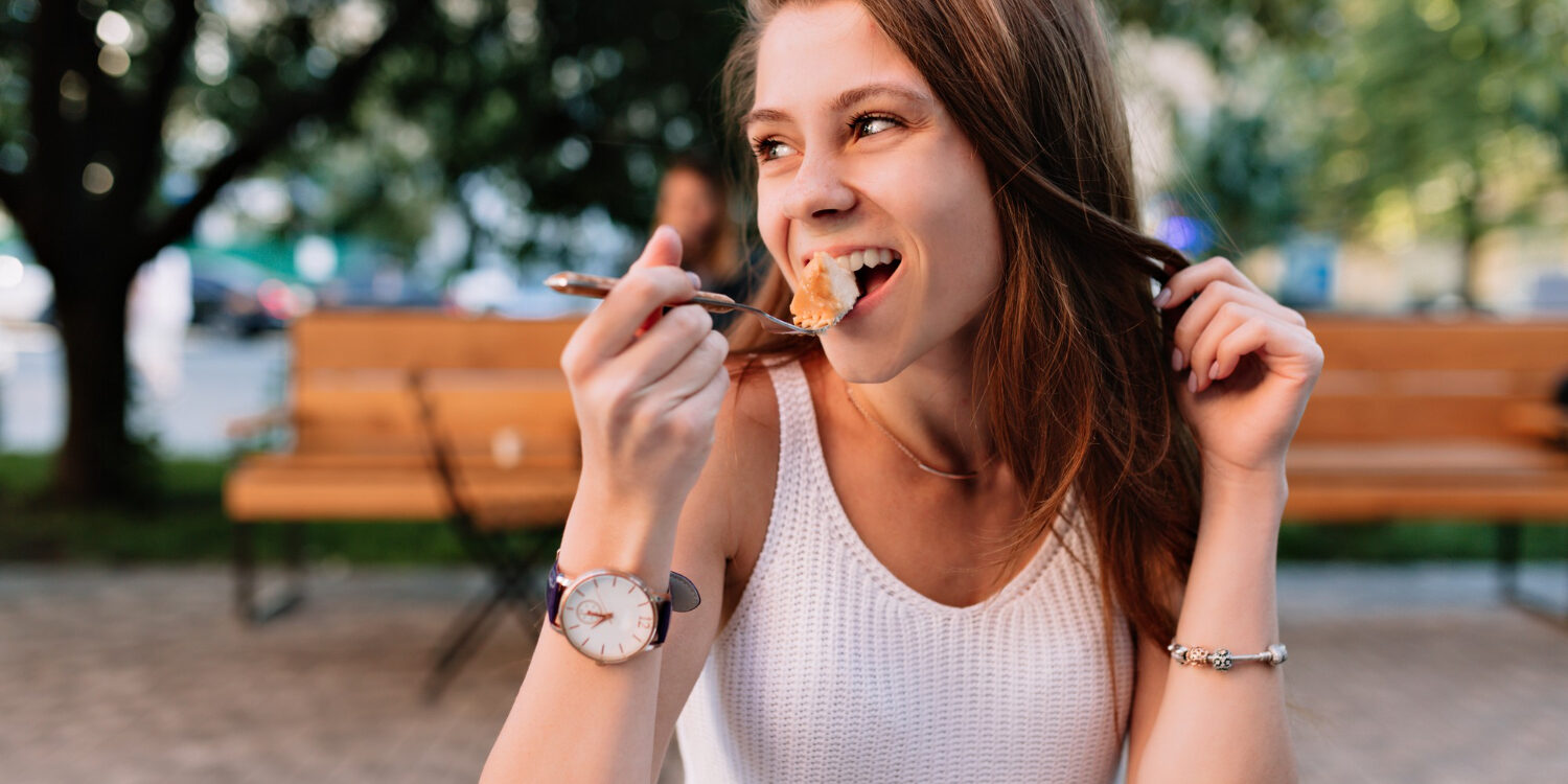 Vrouw in een wit shirt neemt een hap van haar eten en doet aan Goed kauwen voor een gezond gebit
