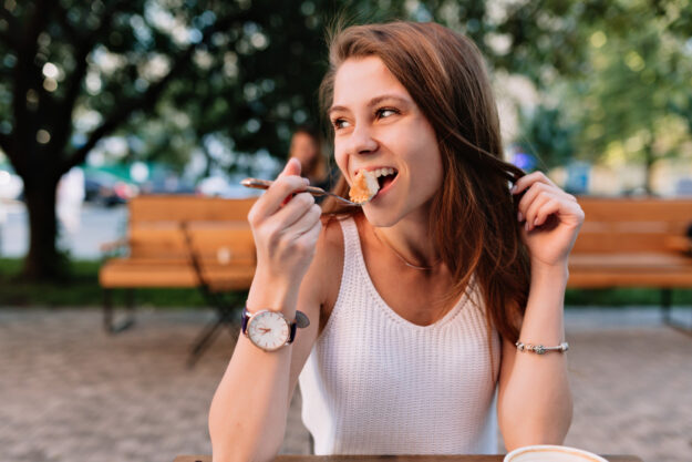 Vrouw in een wit shirt neemt een hap van haar eten en doet aan Goed kauwen voor een gezond gebit